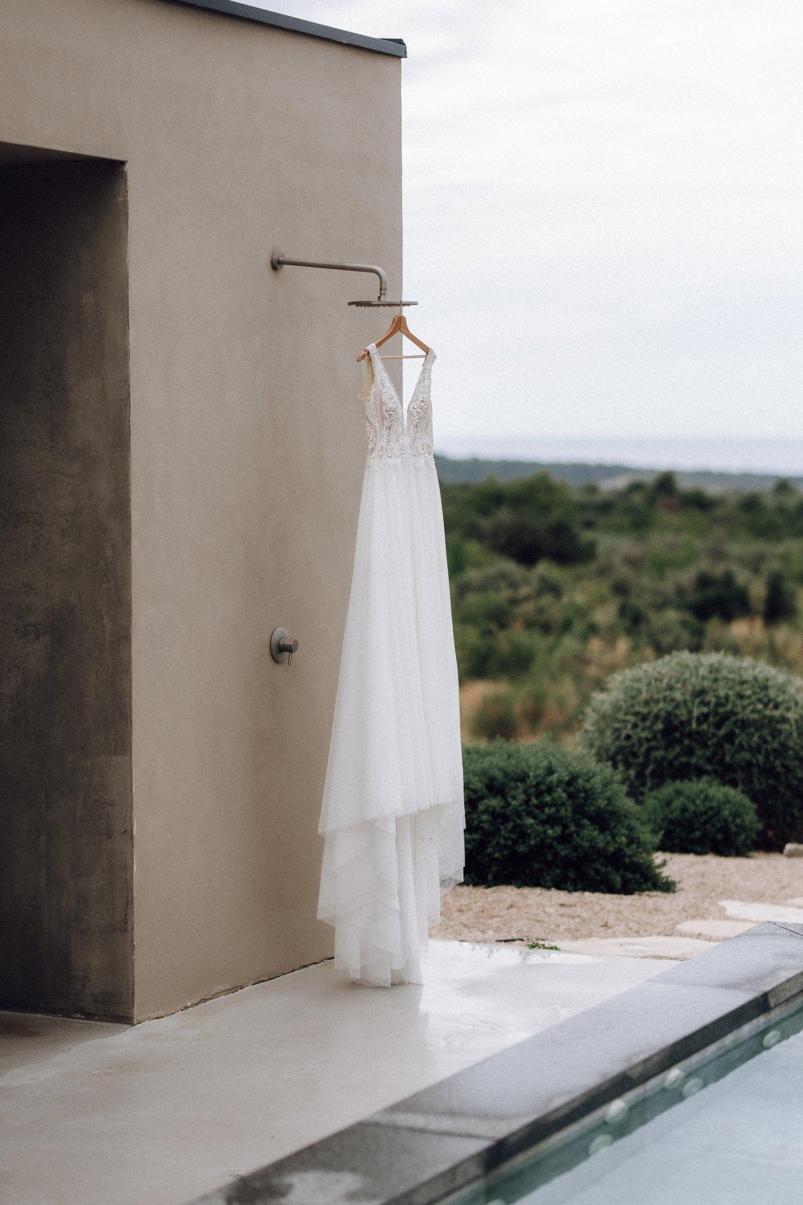 Das Brautkleid hängt an der Außendusche, dahinter wachsen Büsche