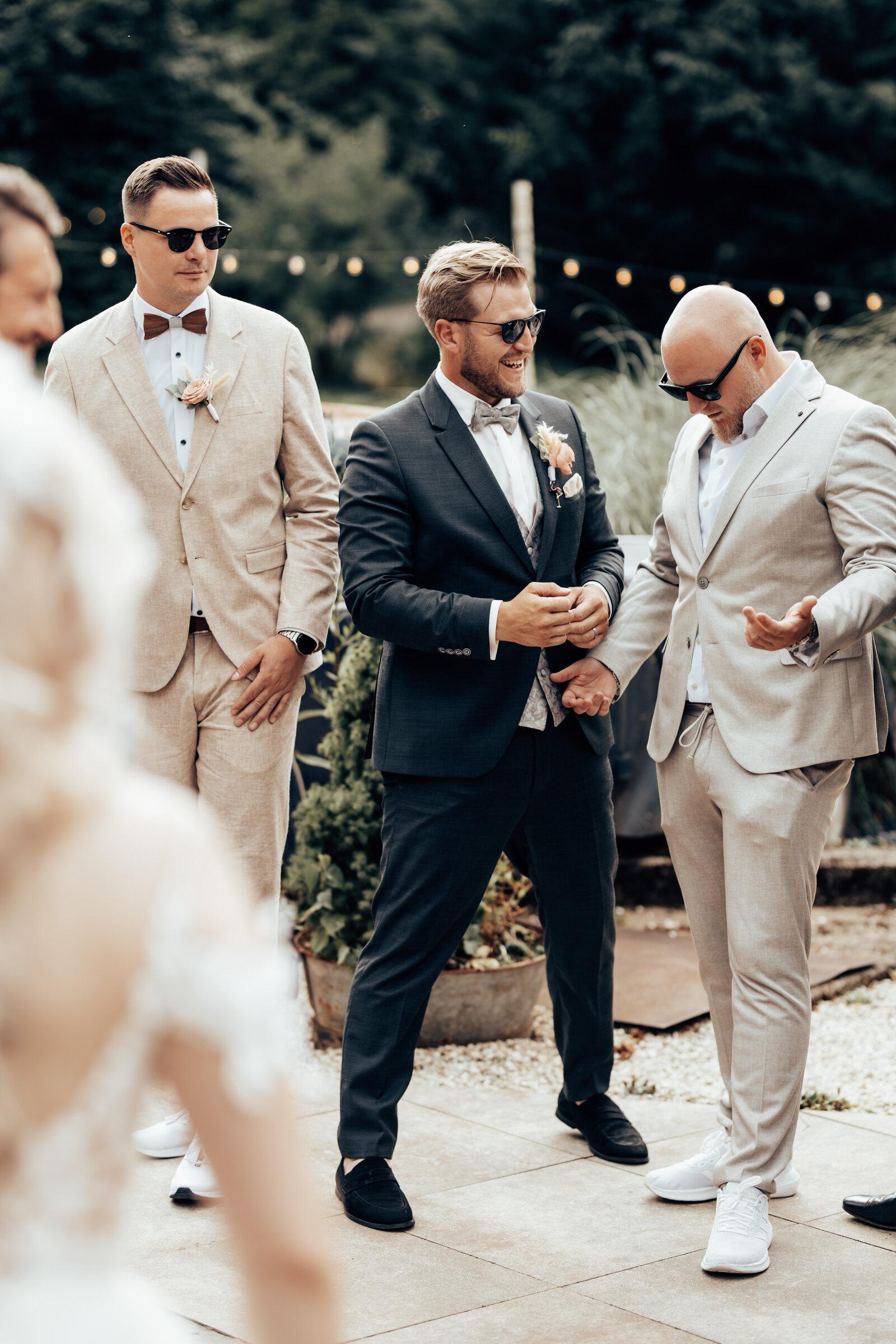 Groom in a dark suit laughing with two witnesses in the garden