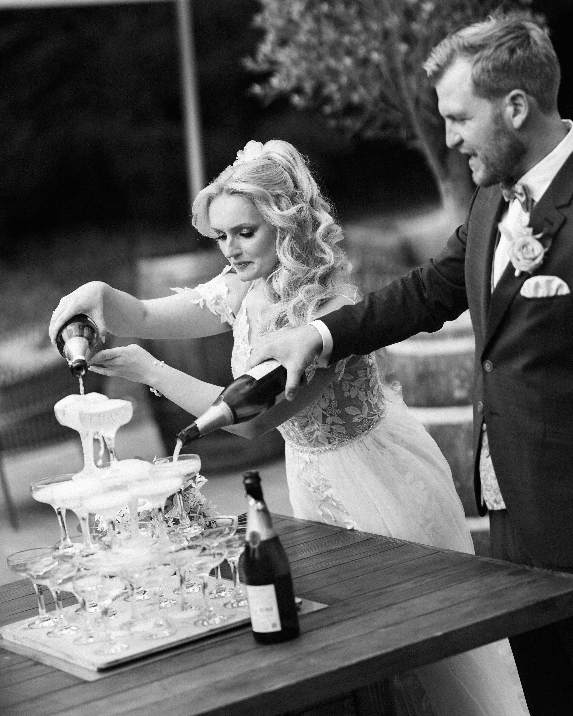 Couple pouring sparkling wine into a champagne tower, black and white