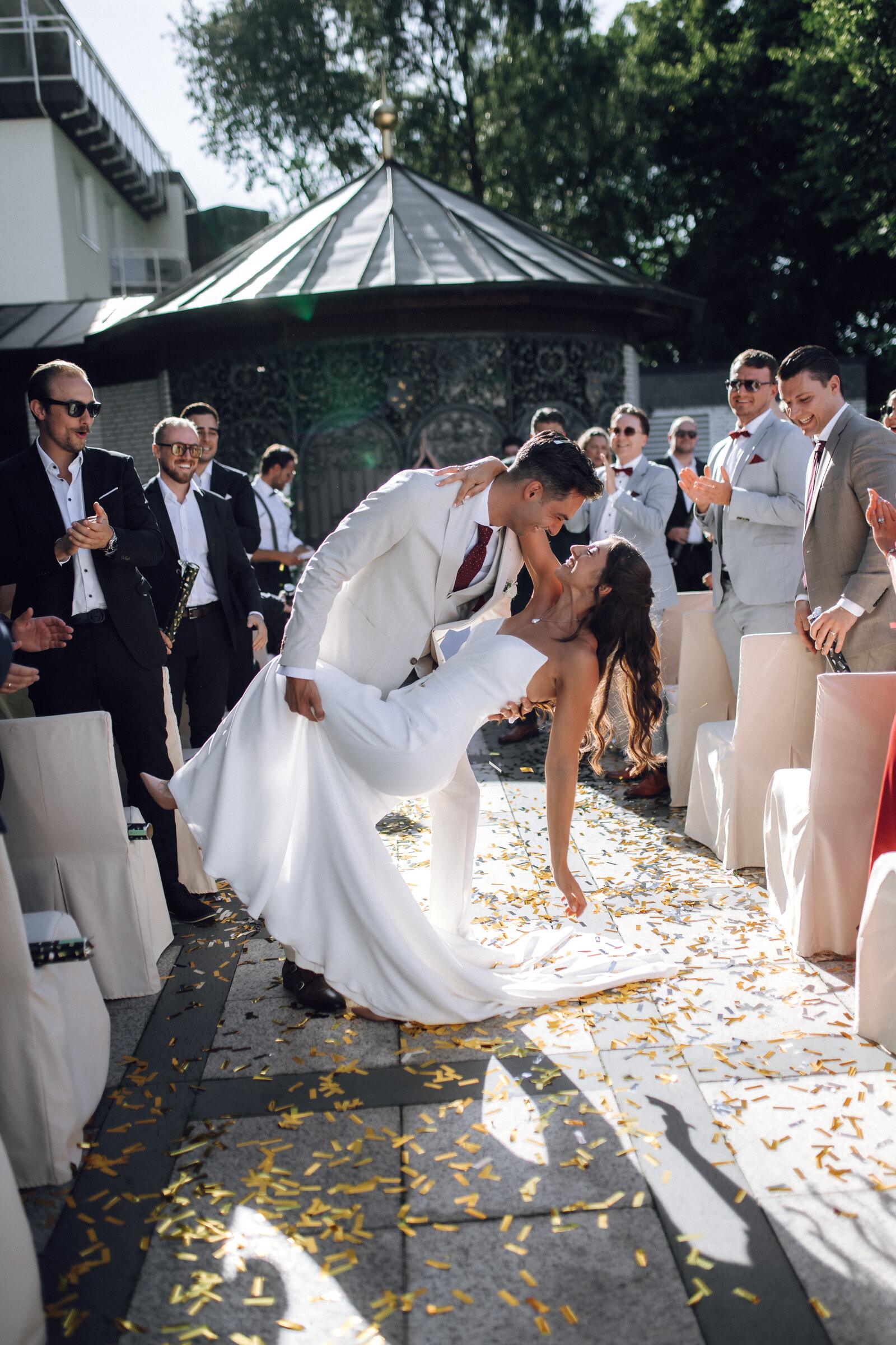 Couple kissing as they walk through a line of guests and confetti
