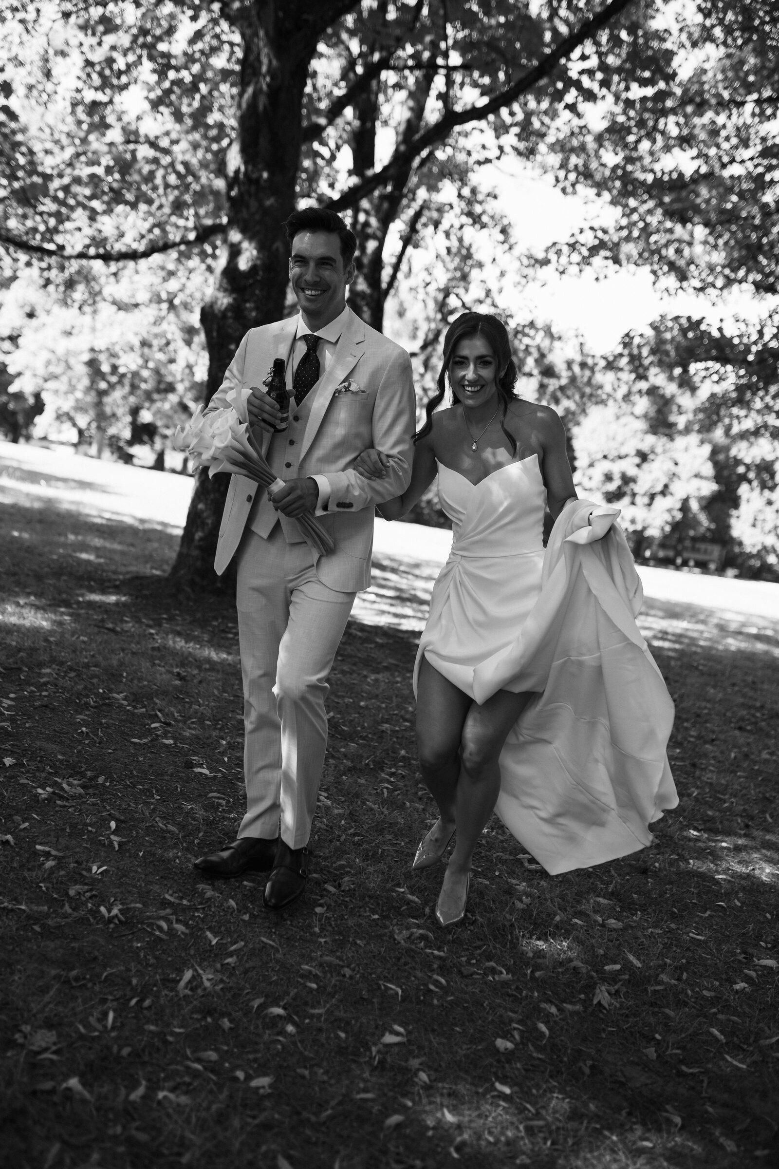 Couple running and laughing through a park, the bride lifting her dress, black and white