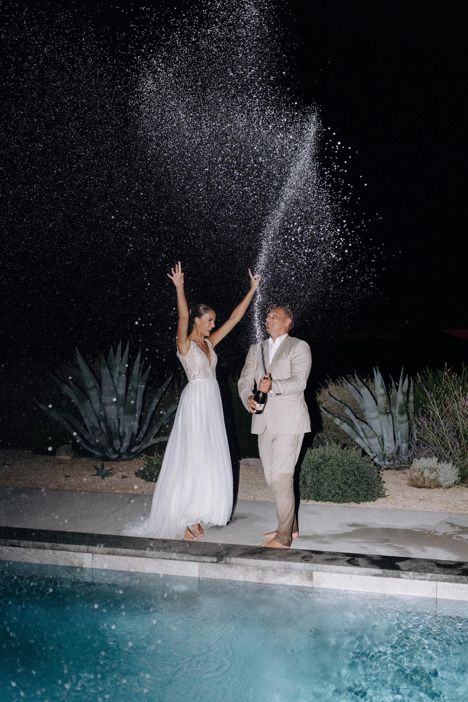 Couple spraying a champagne fountain into the air at the pool at night