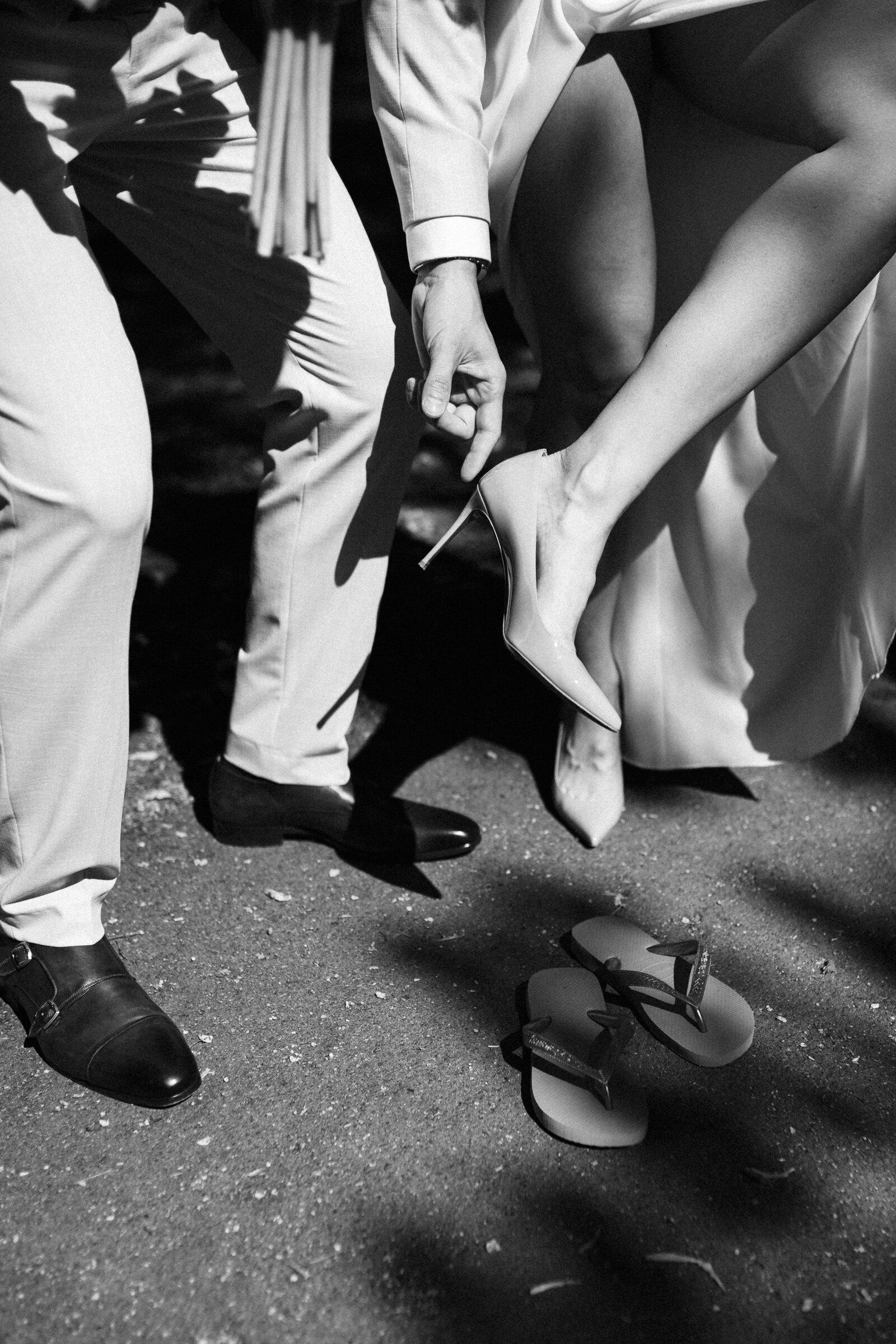 Detail: the bride taking off her heels, black and white