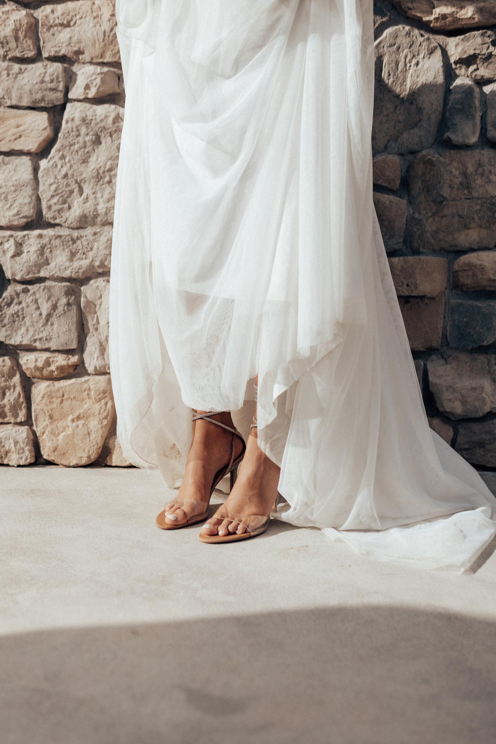 Detail: wedding dress and shoes by a stone wall