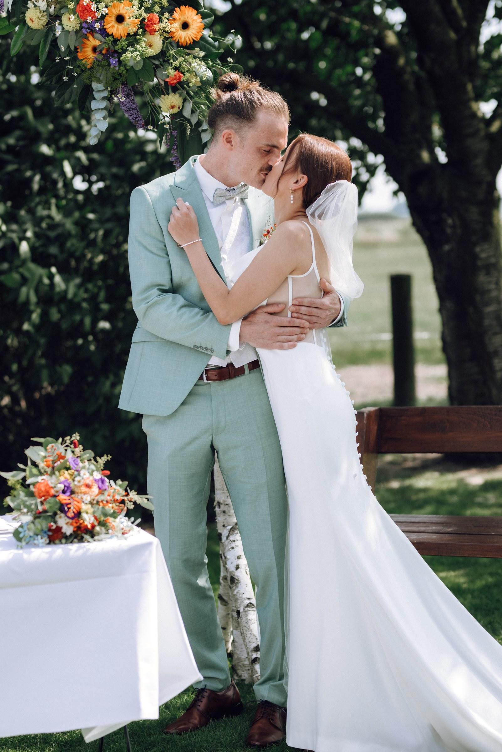 Celine und Philipp umarmen sich unter dem Blumenbogen, daneben ein Strauß auf dem Tisch