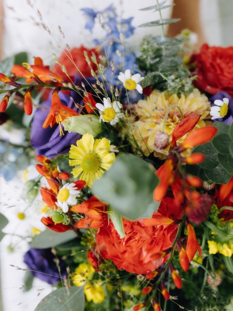 Der bunte Brautstrauß mit roten und gelben Blüten, Kamille und Rittersporn
